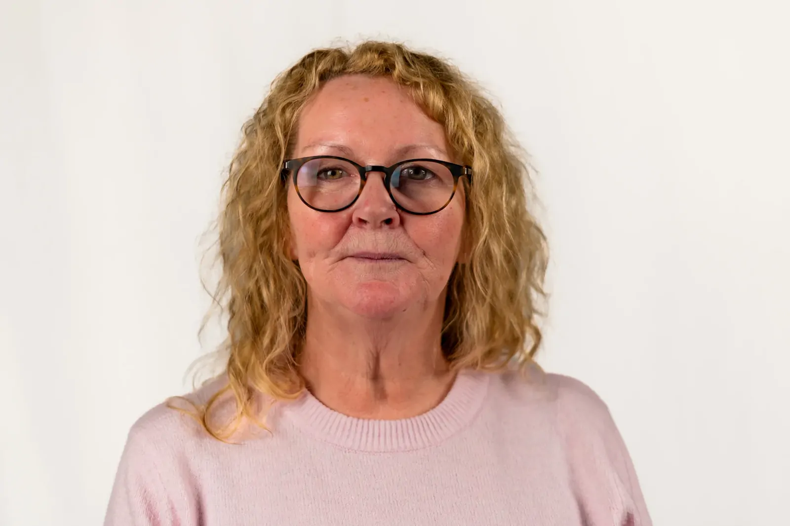 Corporate headshot of a woman with curly hair in a pale pink jumper
