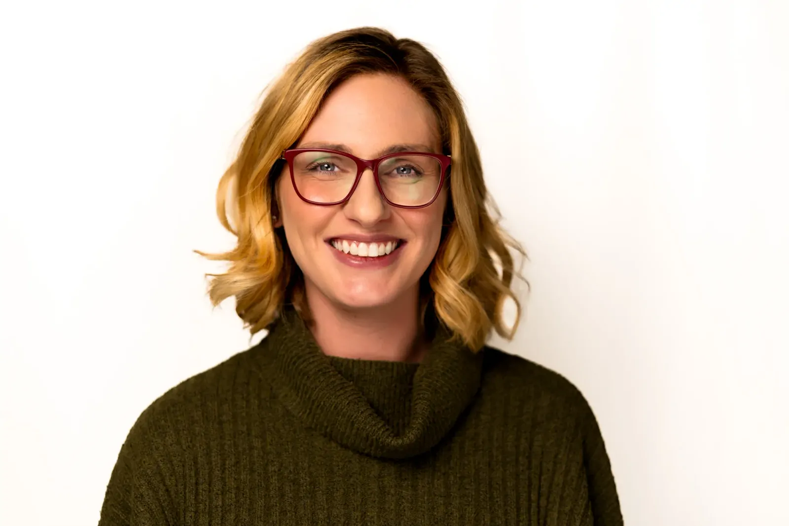 Corporate headshot of a smiling woman in a green turtleneck jumper and red glasses