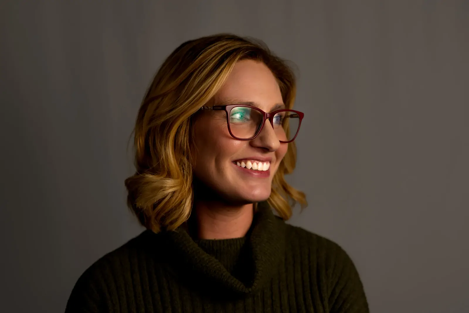 Corporate headshot of a smiling woman in a green jumper with dramatic side lighting