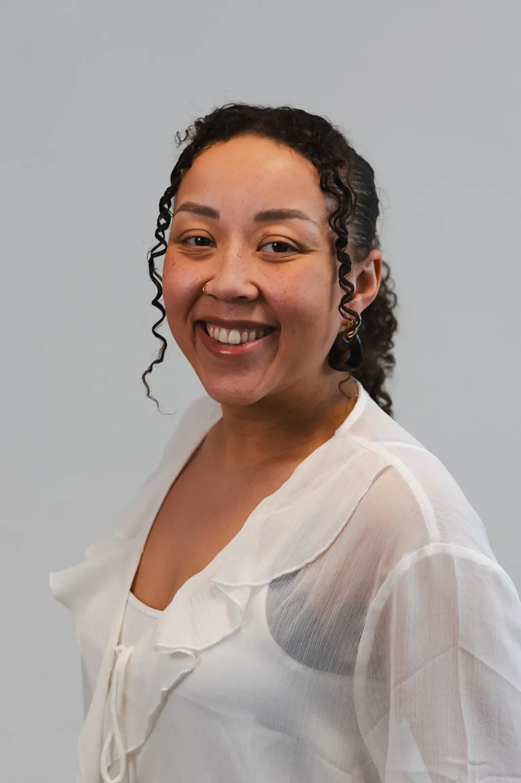 Corporate headshot of a smiling woman in a sheer white blouse, three-quarter view