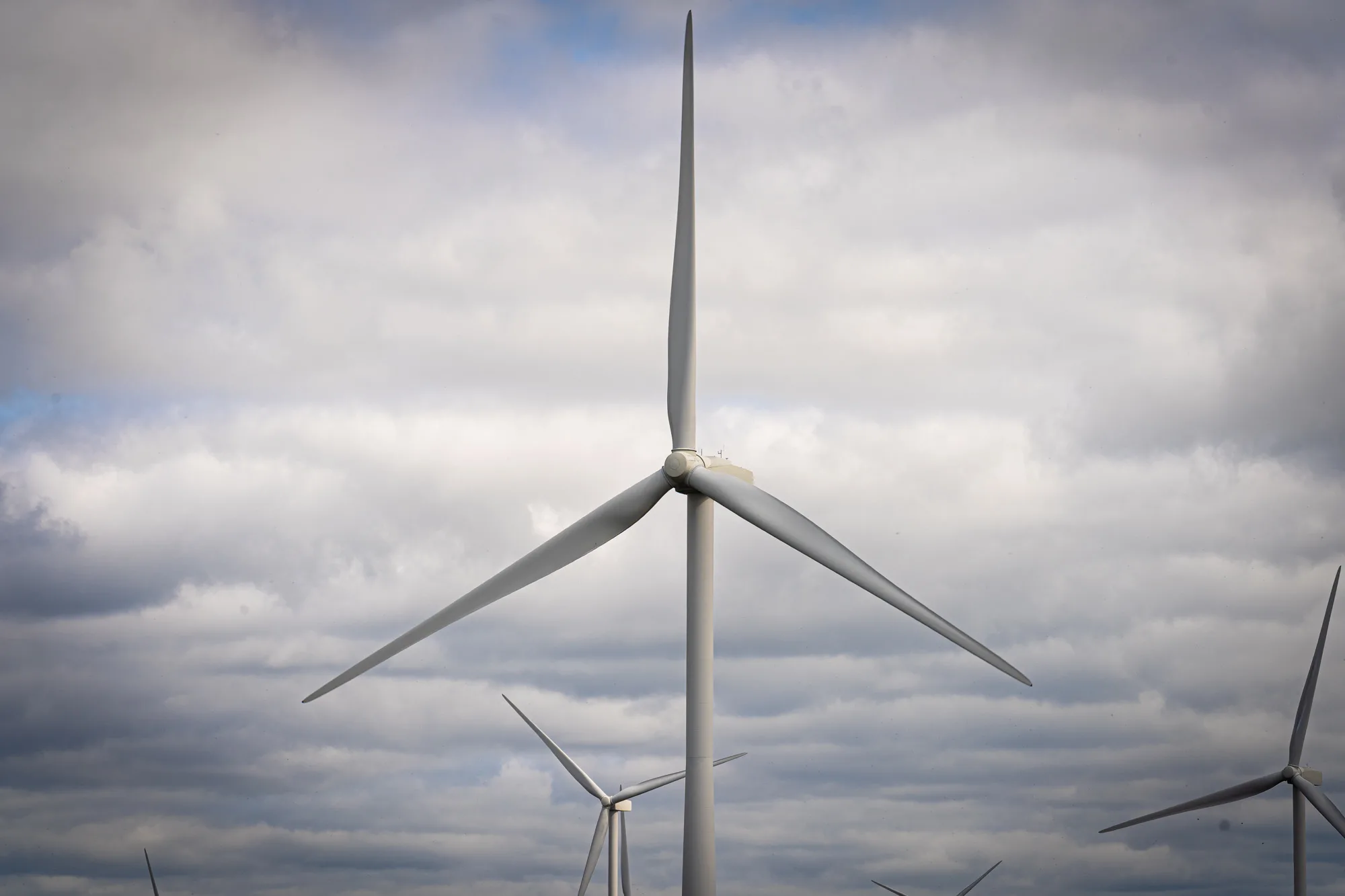 A wind turbine against a cloudy sky with more turbines in the distance