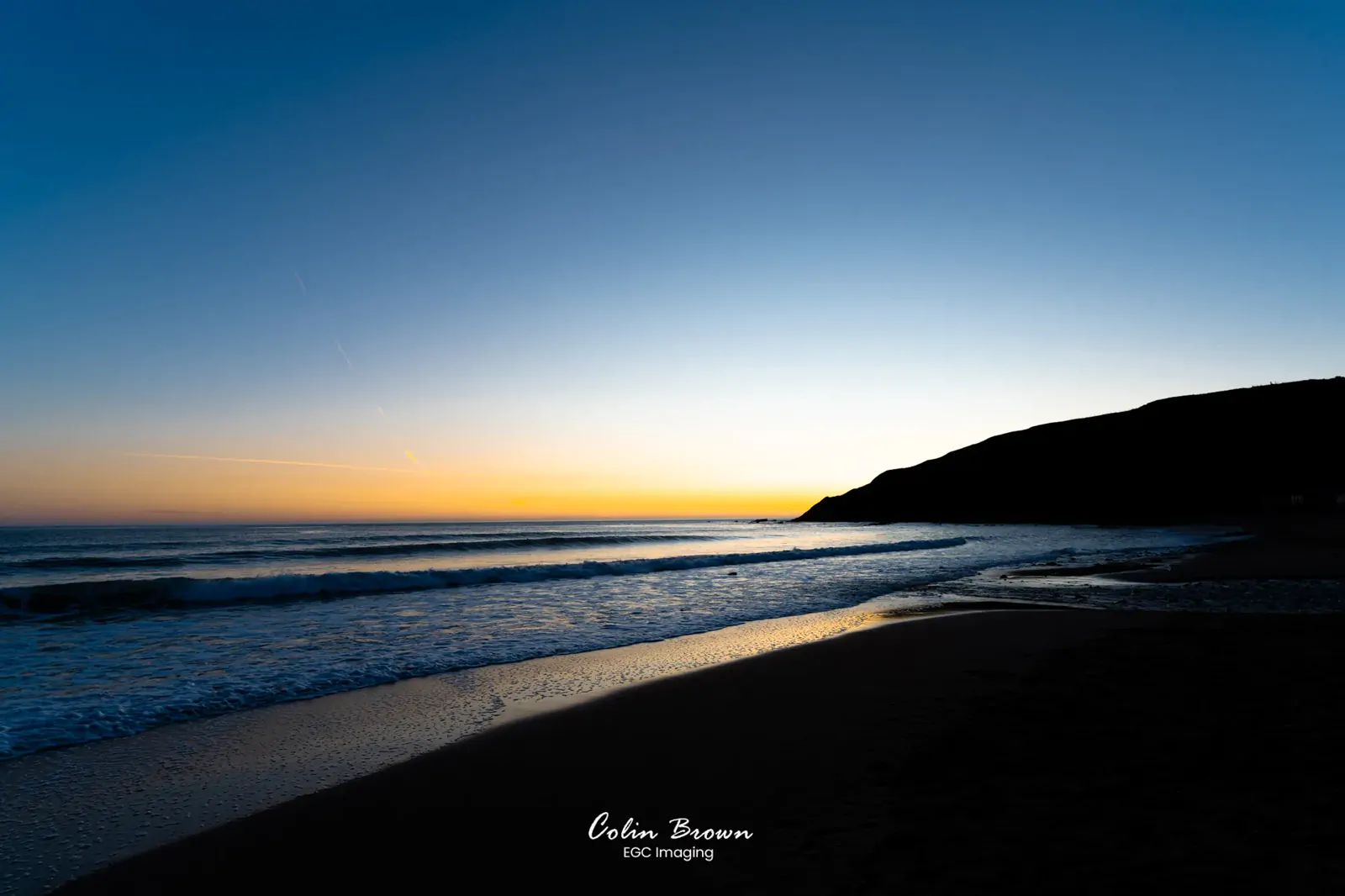 Silhouetted coastal headland at dusk with waves rolling onto the beach