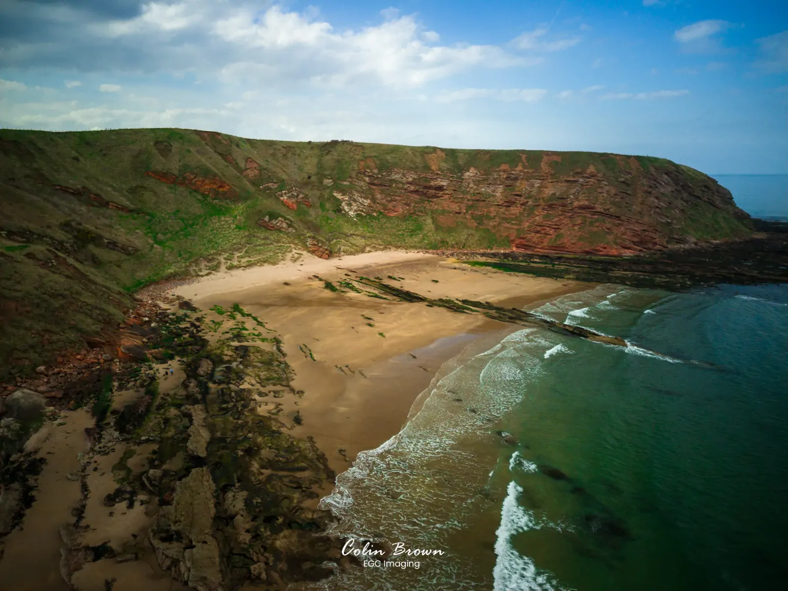 Aerial view of a rocky cove with green and red layered cliffs