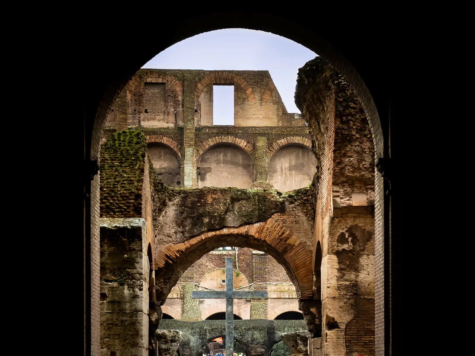 View through a Colosseum archway in Rome, framing a large cross