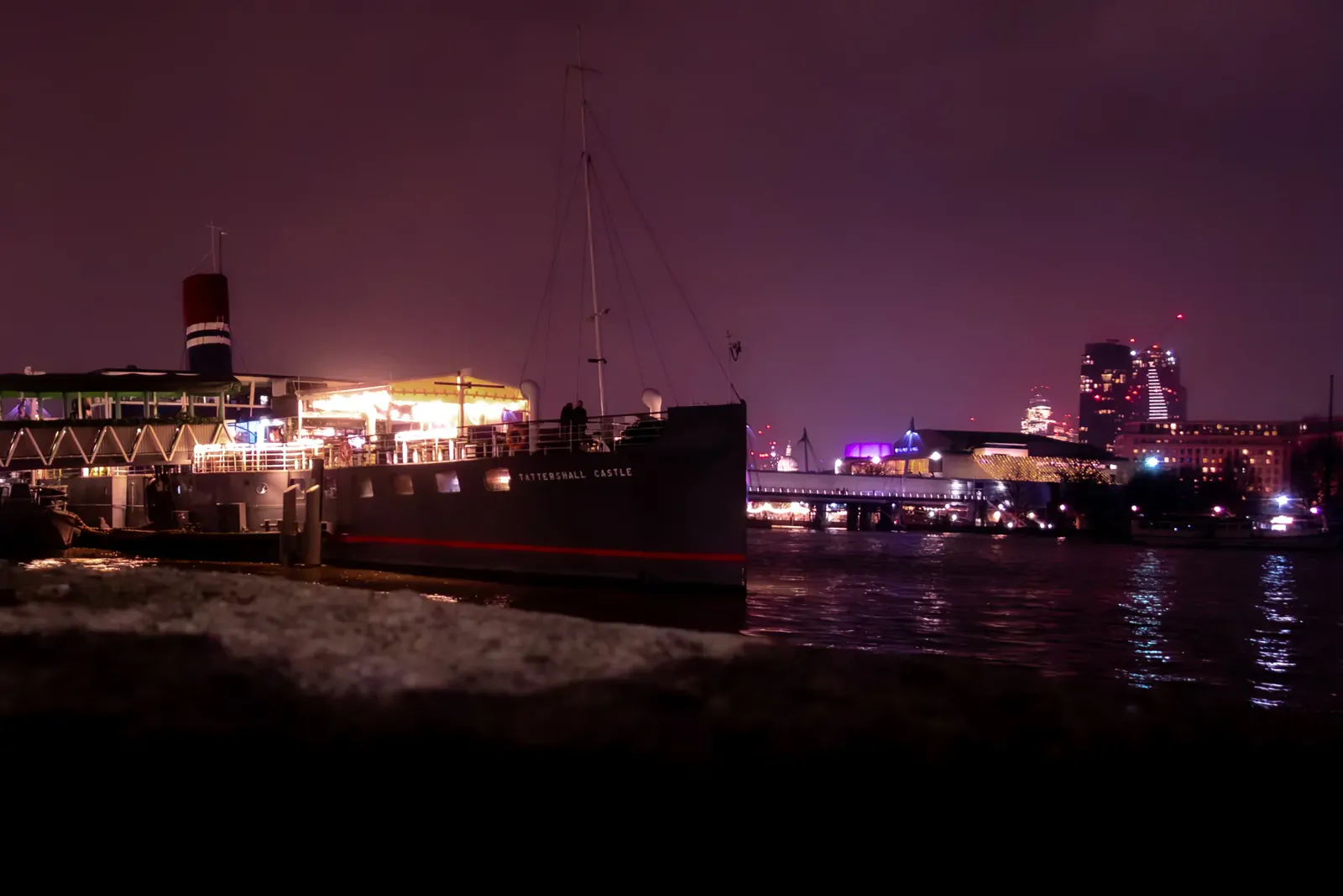 Historic paddle steamer moored on the Thames at night with the London skyline behind