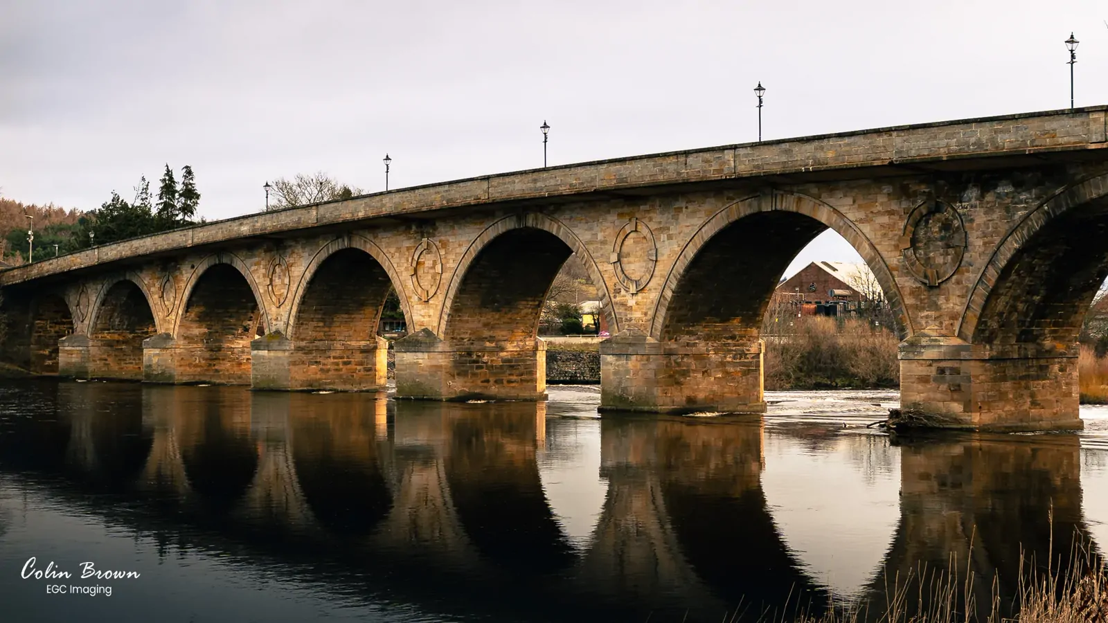 Multi-arched stone bridge reflected in a calm river at golden hour